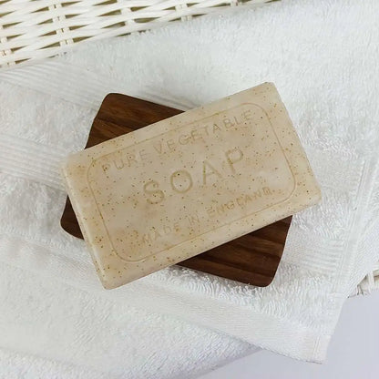 Bar of soap on a wooden soap dish with a white towel in the background