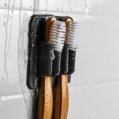 close-up of wet black silicone toothbrush holder with toothbrushes in it on a white tile background.