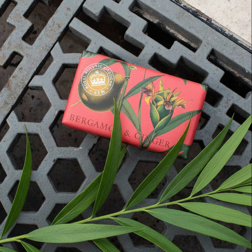 bar of soap with floral and fruit printed wrapper laying on a metal surface with green leaves