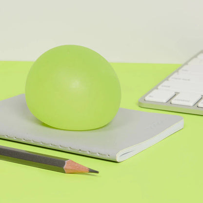 yellow stress ball on a notebook with a pencil and keyboard in the background on a green surface