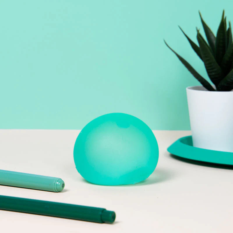 green stress ball set on a desk with pens and a small plant