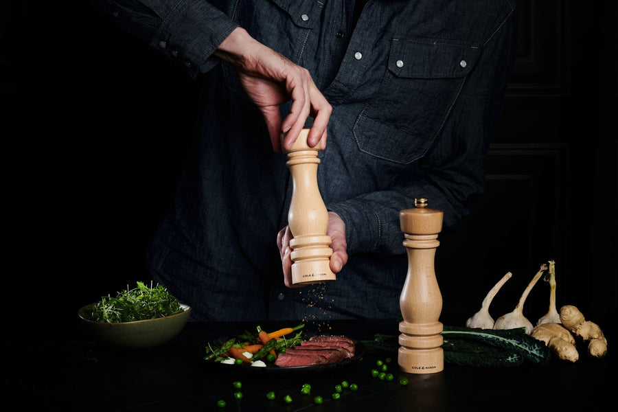 person holding mill over plate of food grind salt on to it with another mill set next to it.