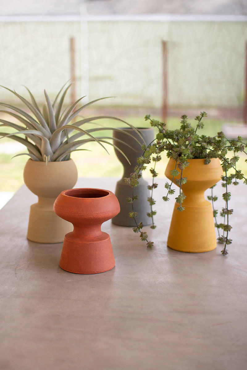 4 sizes and colors of rounded pedestal vases on  a concrete table, 2 vases have succulents in them.