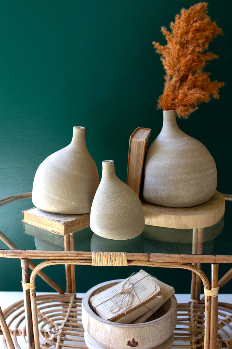 3 sizes of teardrop vases set on a table with books, largest vase has an orange plume in it.