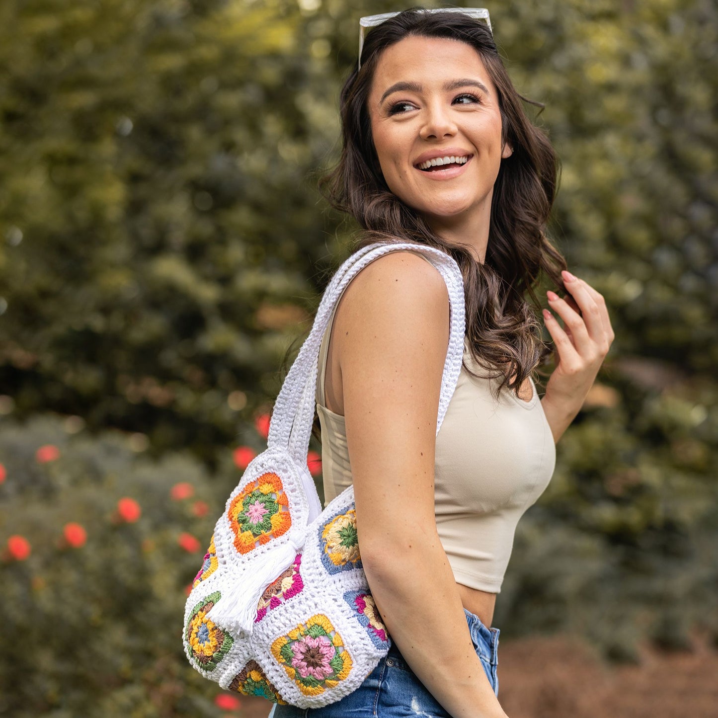 person walking in park with a white purse made of colorful crochet granny squares on their shoulder.