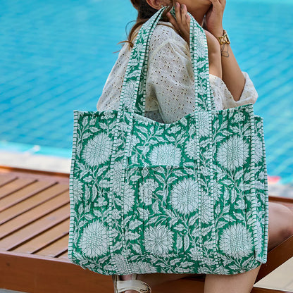 Person holding a green and white floral patterned tote bag by a pool.