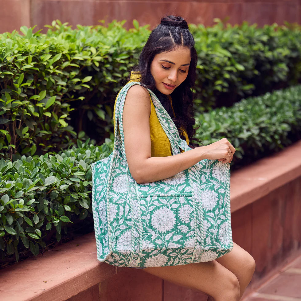 Woman holding a green and white patterned tote bag outdoors.