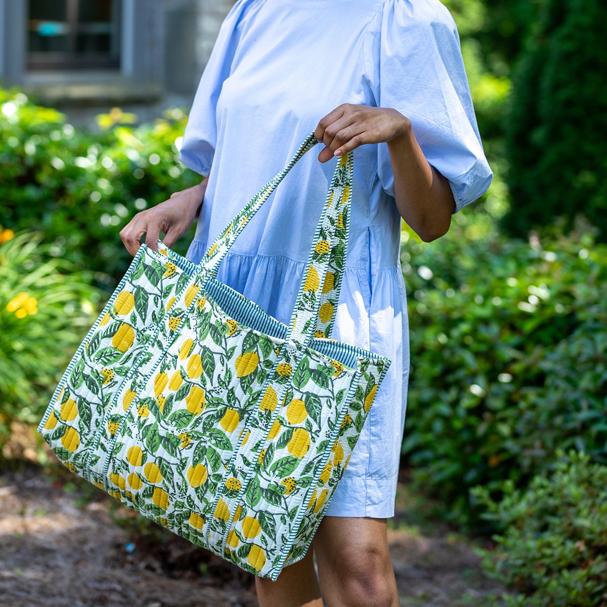 Person wearing a light blue dress holding a green and yellow lemon patterned bag in an outdoor setting