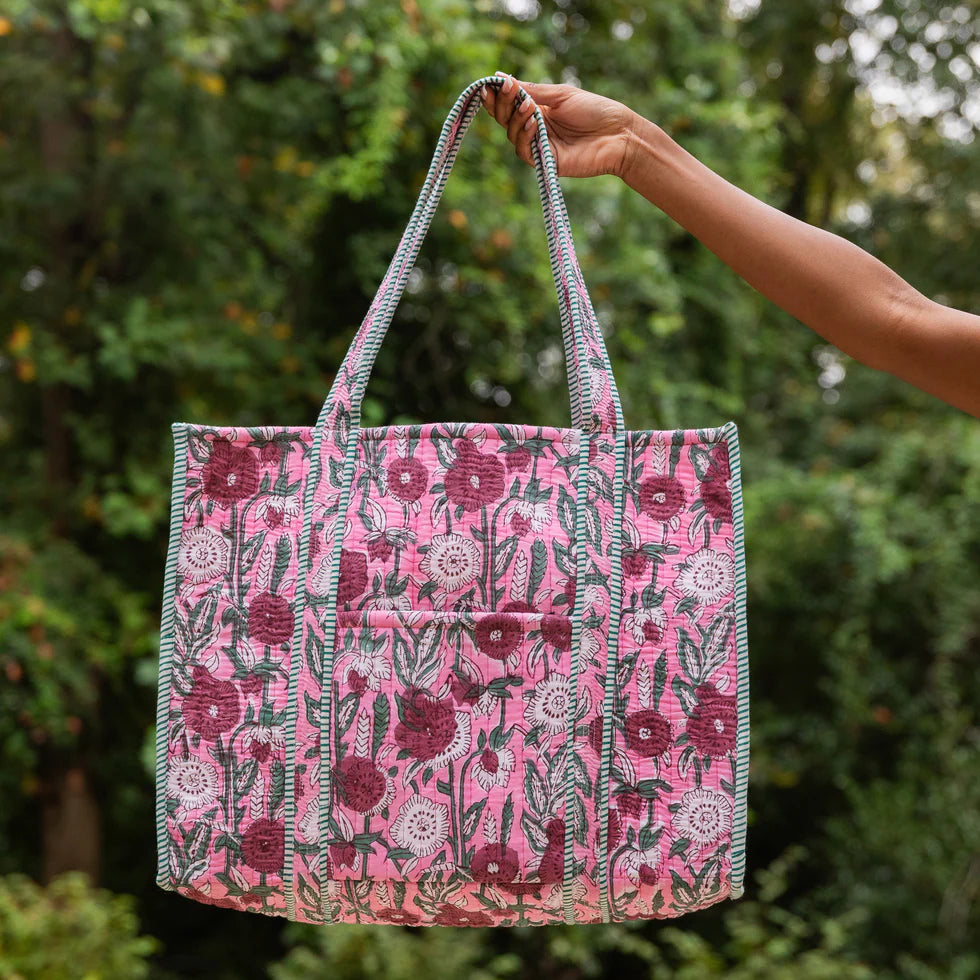Hand holding a pink floral patterned bag against a green leafy background