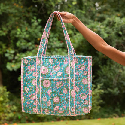 Hand holding a floral patterned tote bag against a green outdoor background