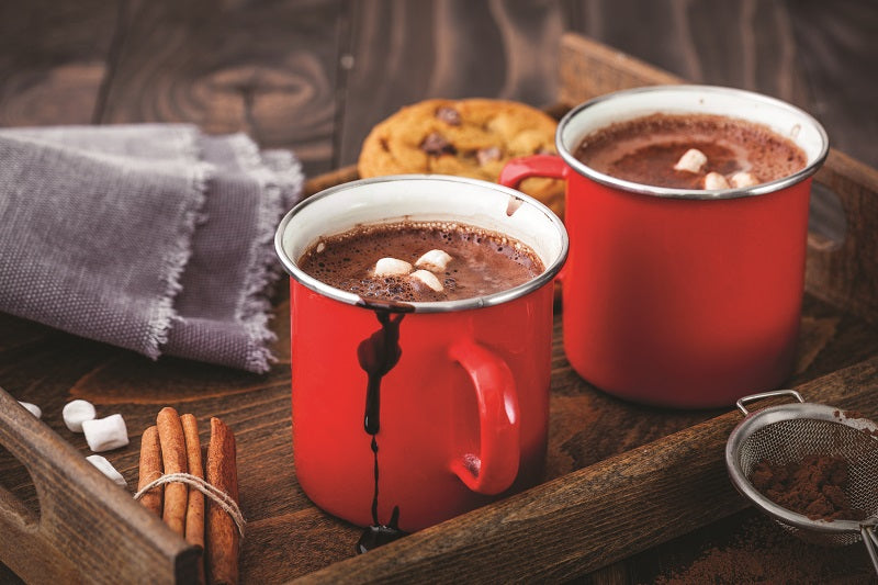 2 red mugs filled with cocoa topped with marshmellows set on a wooden tray with spices, cookies, and a napkin.
