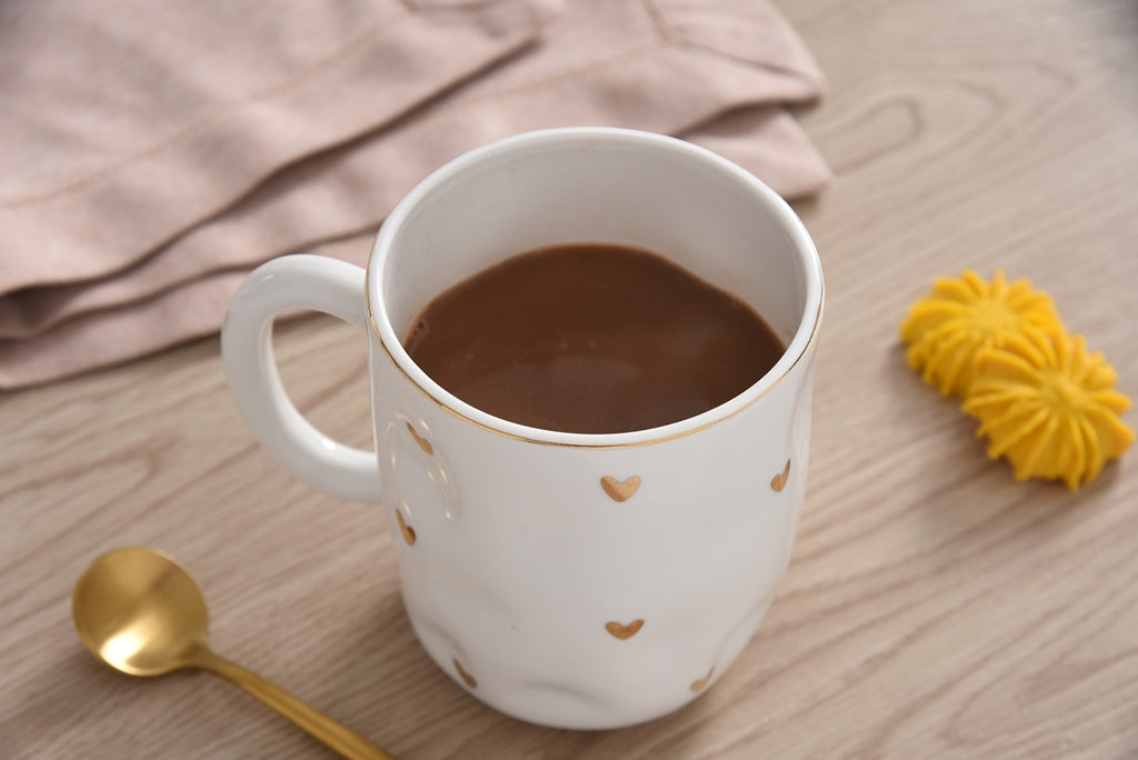 white mug with gold hearts on it filled with beverage
