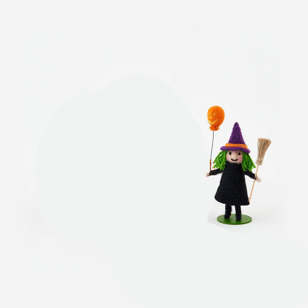 small felt figurine a child dressed in witch costume with purple hat holding an orange balloon