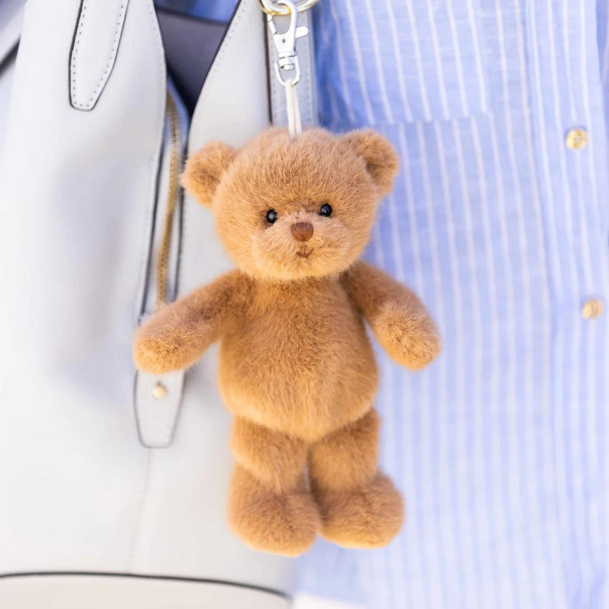 mavi bear bag charm clipped onto an off-white purse