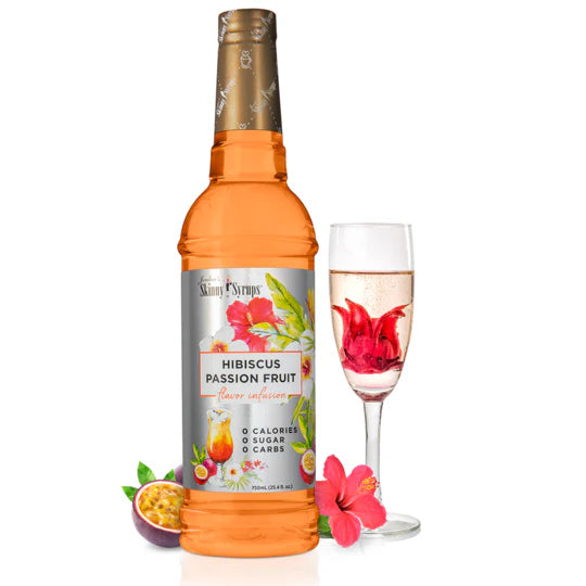 bottle of Hibiscus Passion Fruit skinny syrup set next to a stemmed glass with a beverage and flower in it.