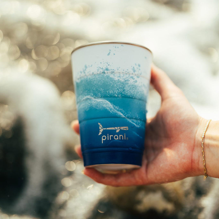 hand holding Tsunami tumbler with ocean in the background.