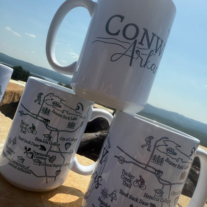 stack of conway arkansas mugs with a scenic arkansas view in the background
