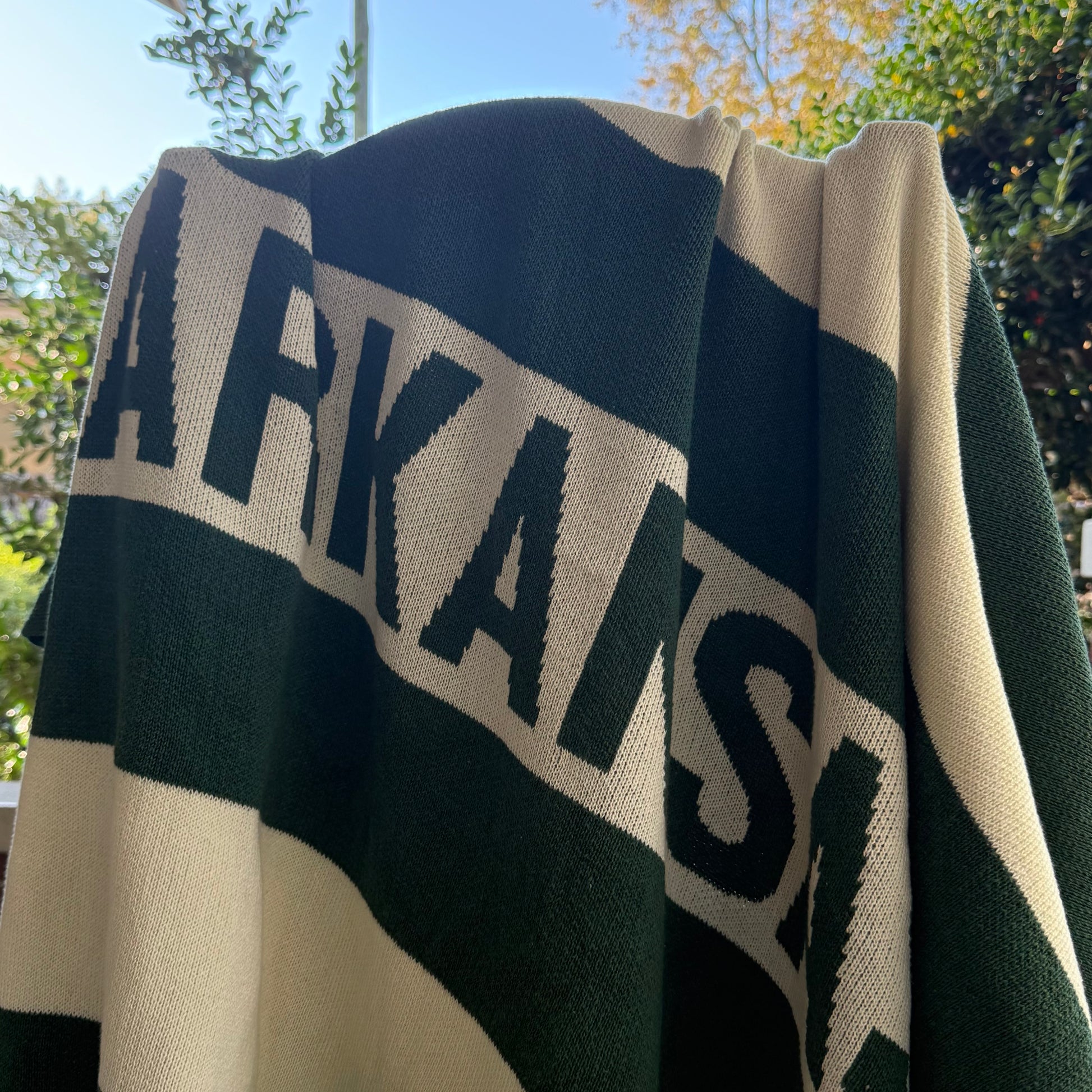 green and off-white knit Blanket with 'ARKANSAS'  text on it draped over a chair outdoors