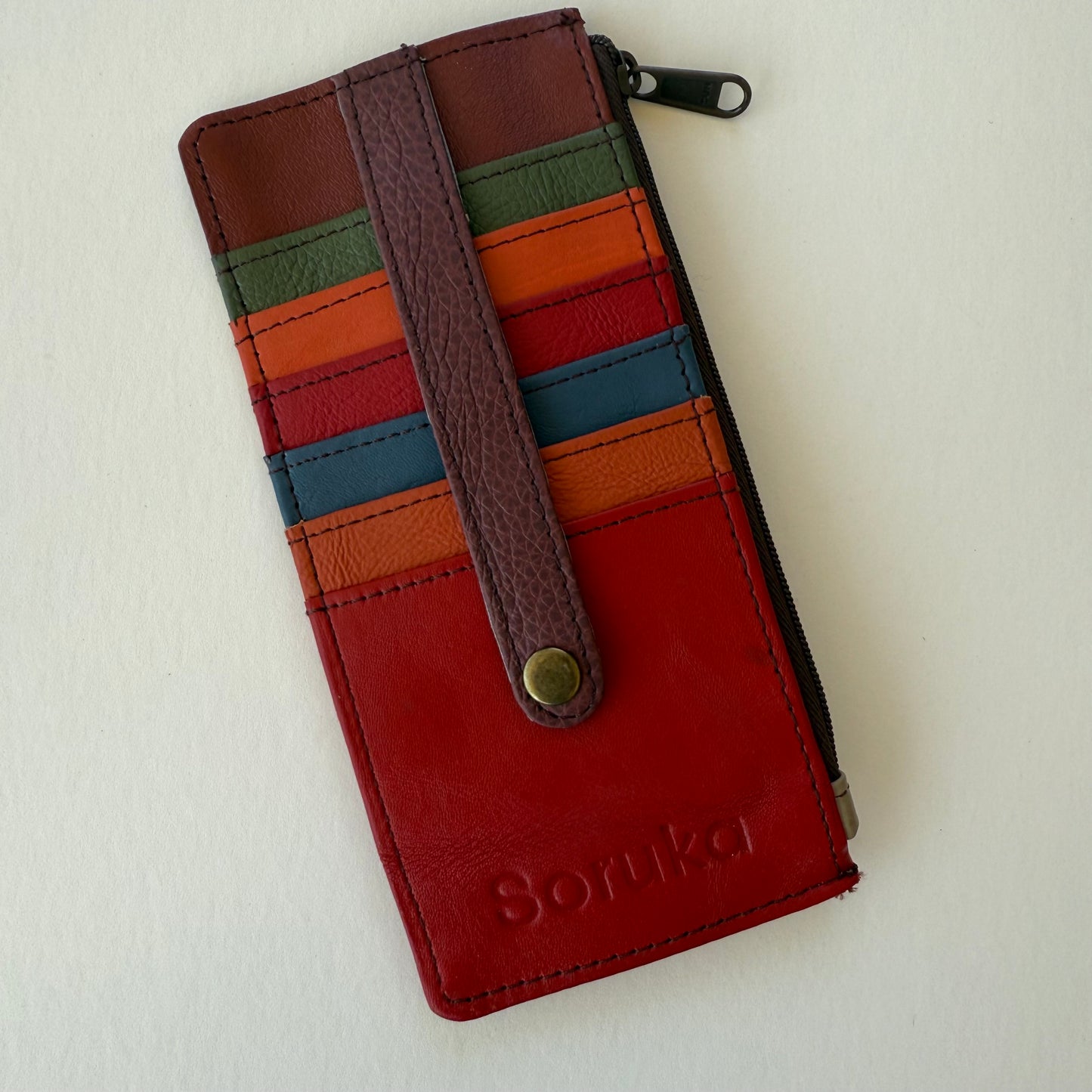Red leather wallet with colorful cards slots and strap on a white background