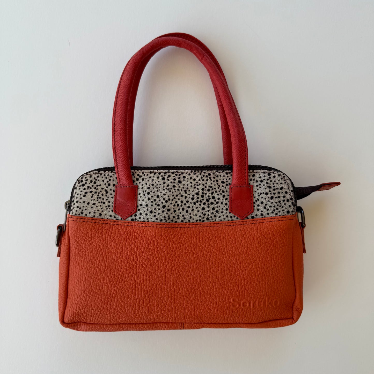 orange handbag with black and white pattern and orange handles shown on a white background