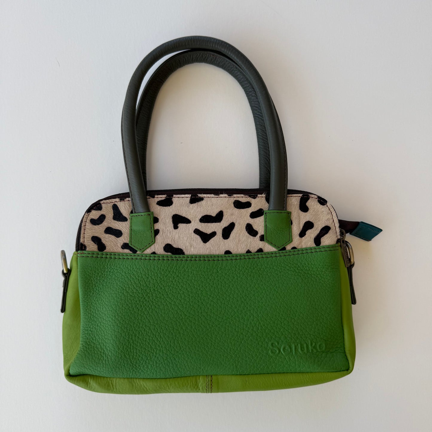green leather handbag with black and white spotted accent and dark green handles shown on a white background