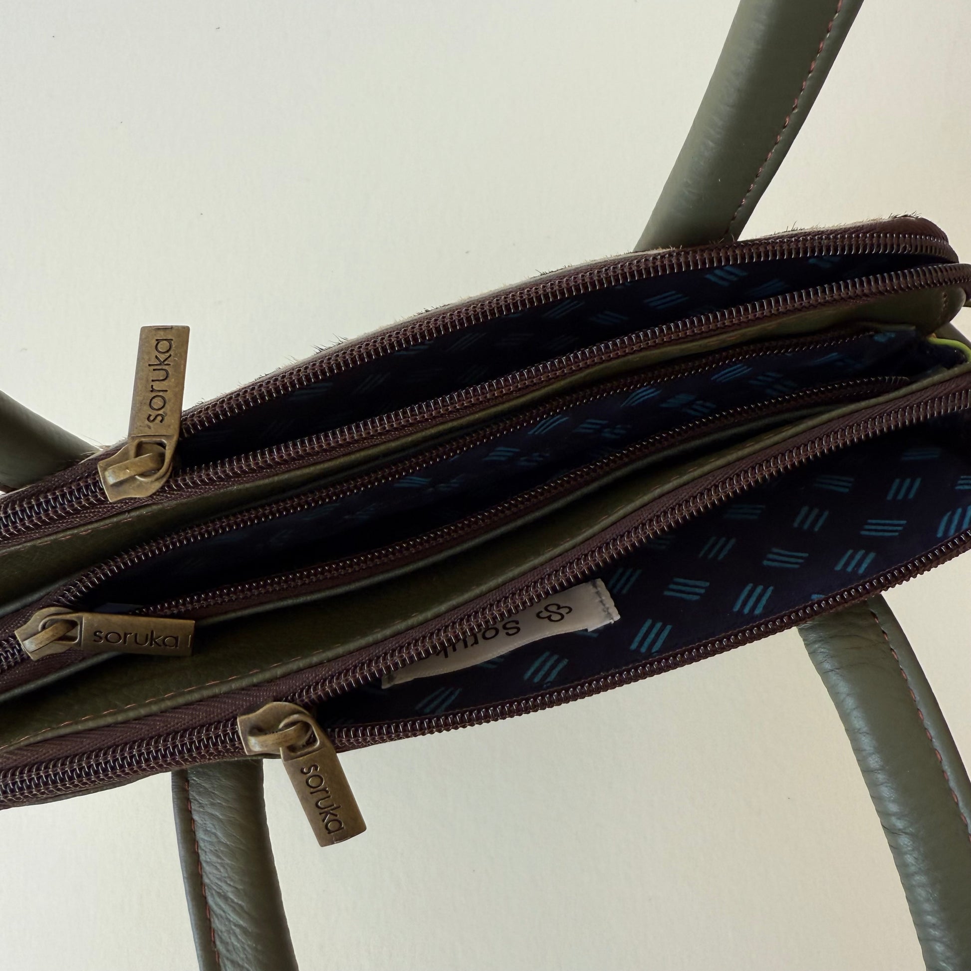 top view of green leather handbag with 3 zippered compartments