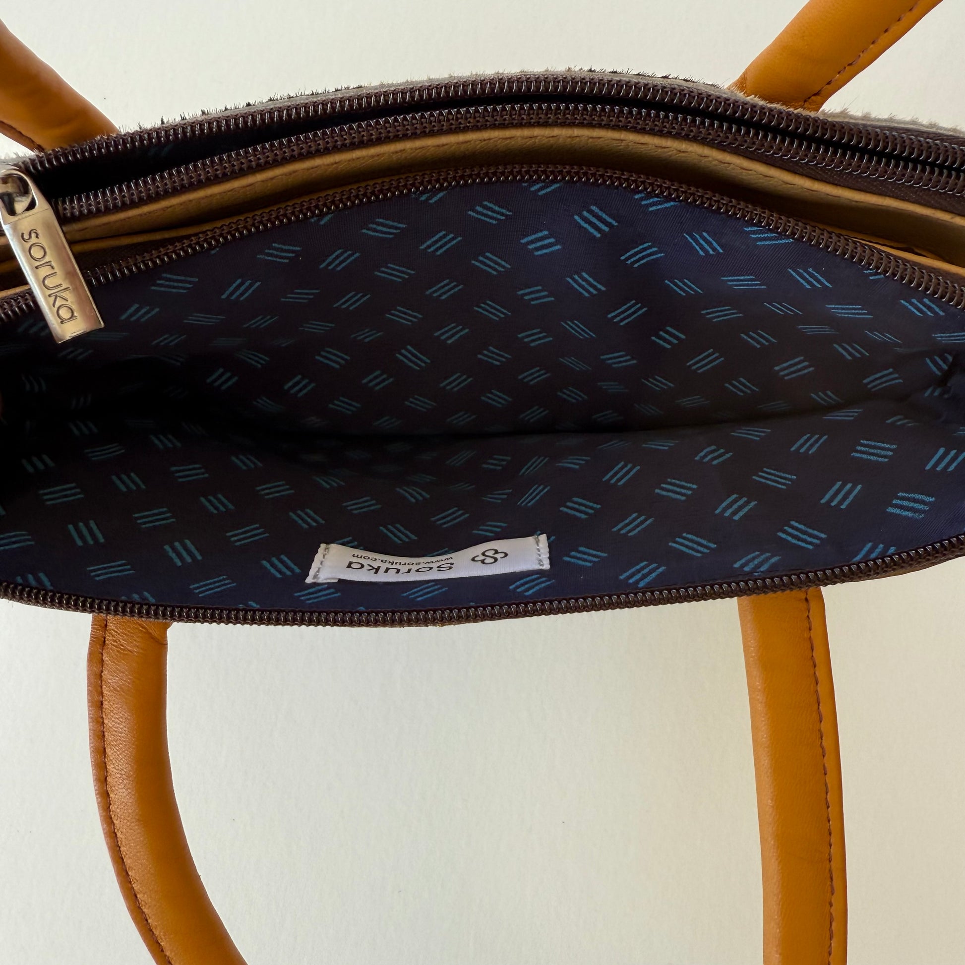 interior top view of wheat colored leather handbag showing blue patterned lining