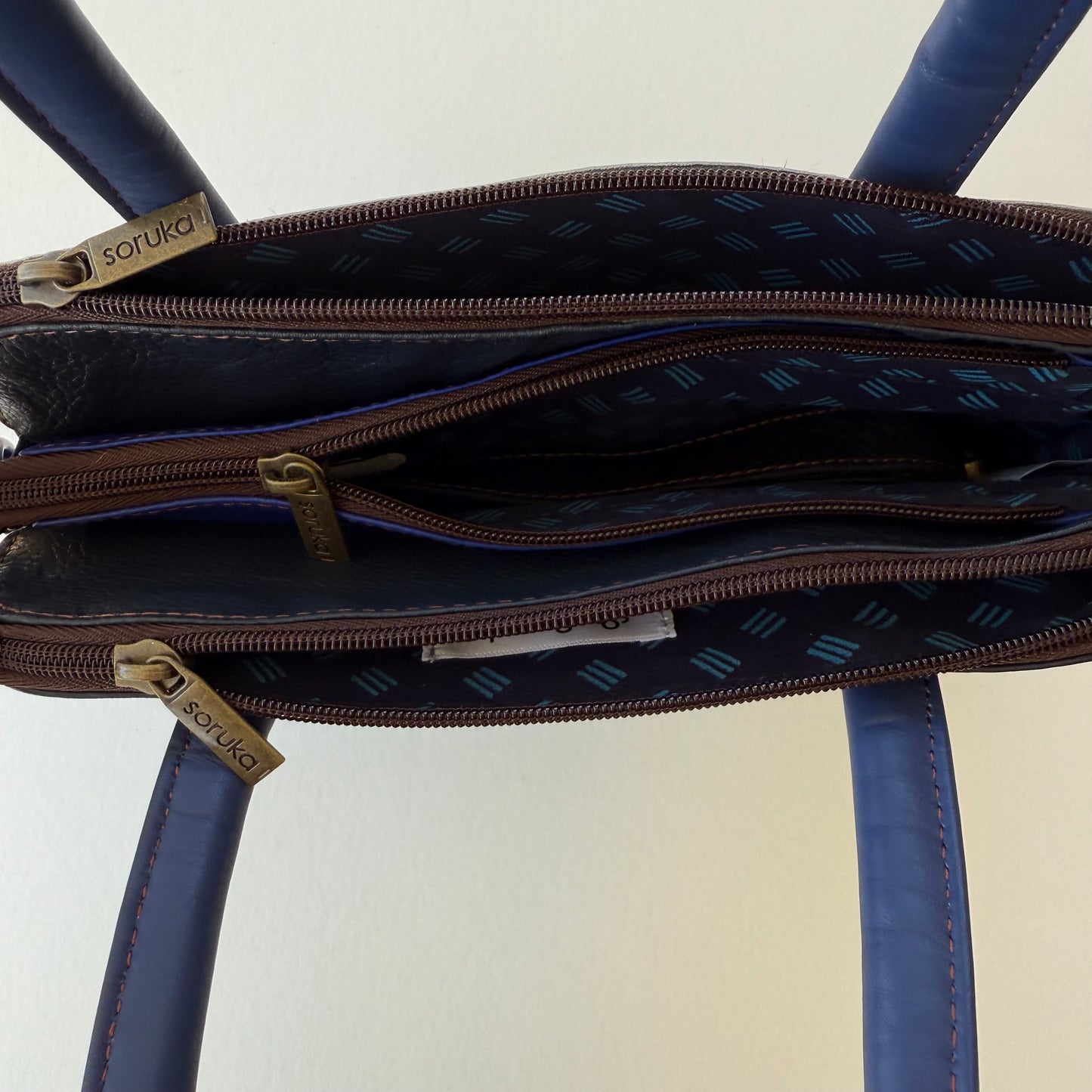 top view of blue leather handbag showing 3 zippered compartments