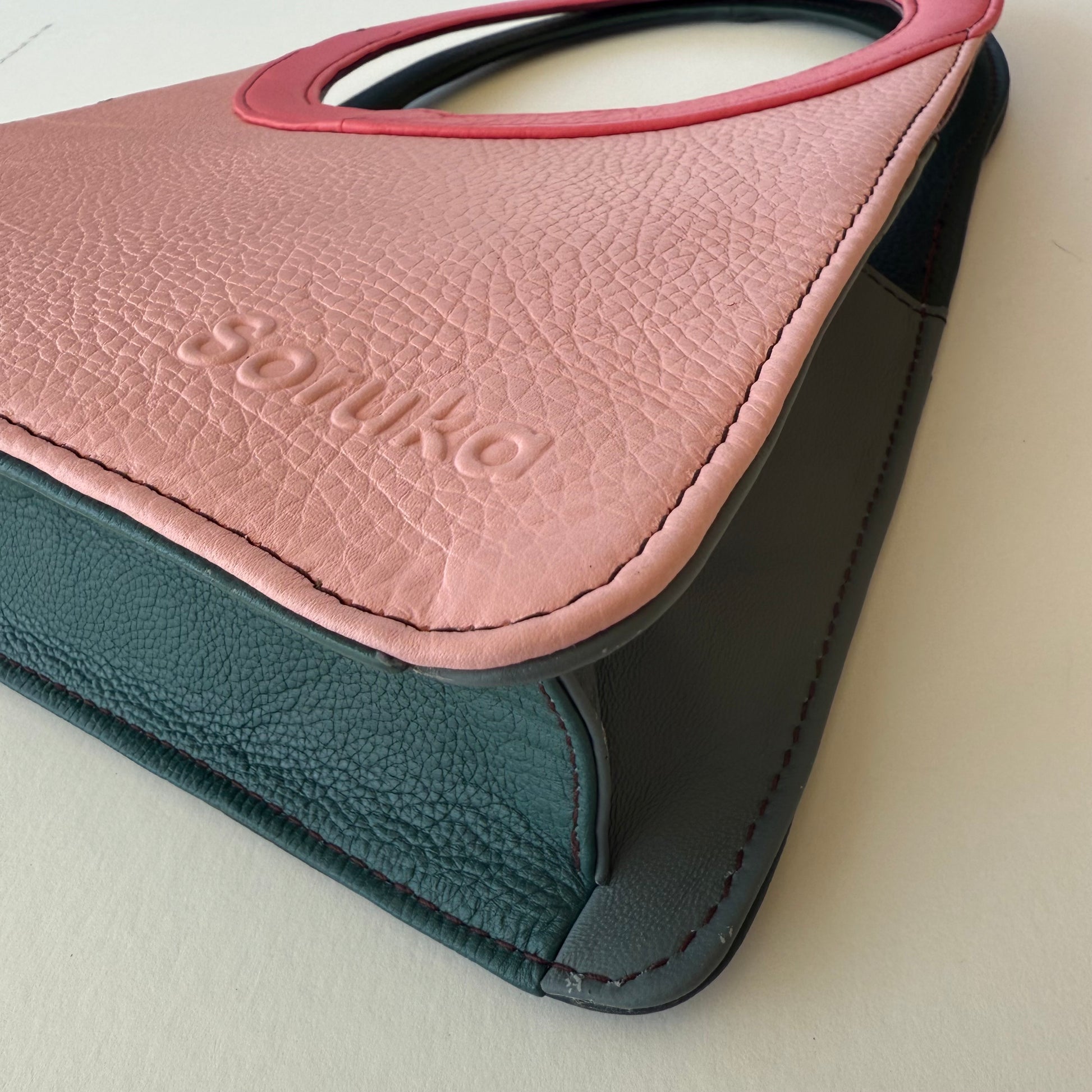 Close-up of bottom corner of a pink and black leather purse on a light beige background.