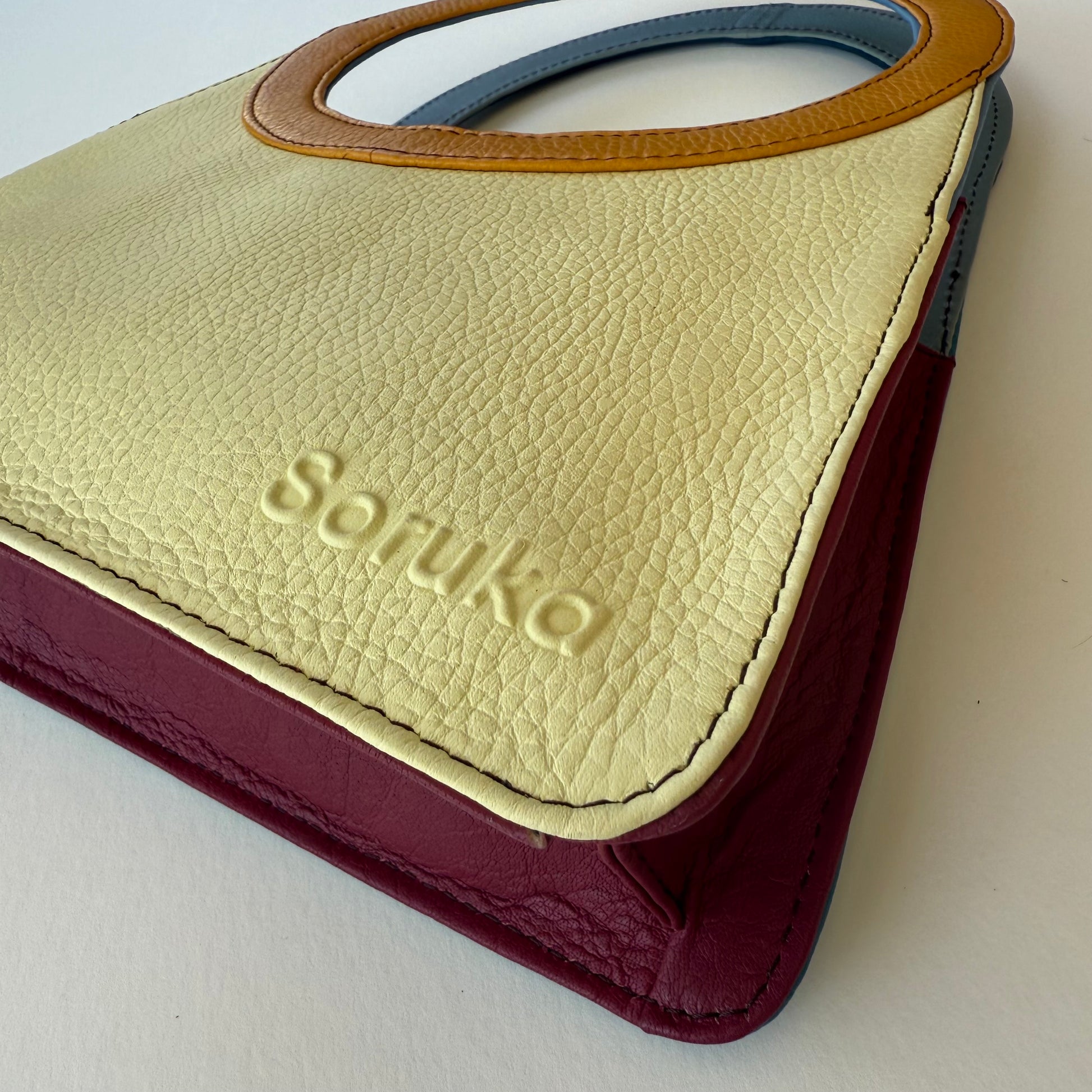 close-up of bottom corner of yellow handbag with maroon base