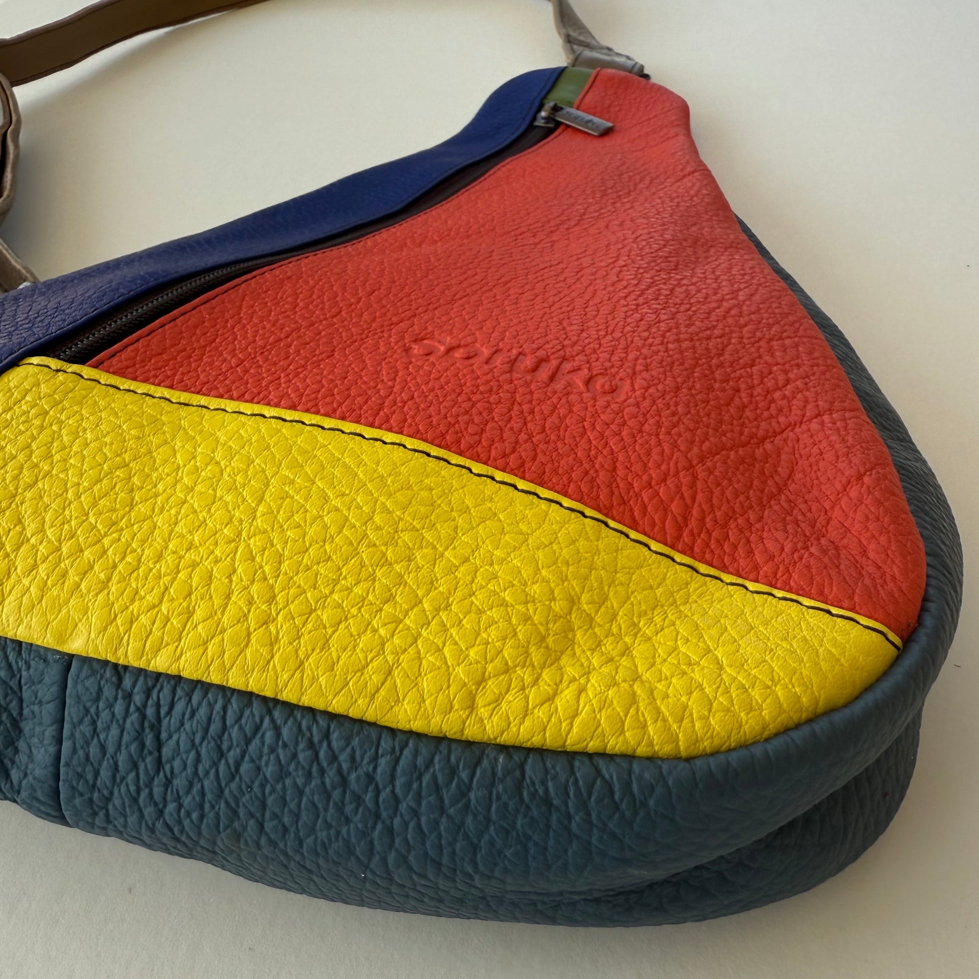 close-up of bottom corner of Colorful leather handbag with red, yellow, and blue sections on a white background