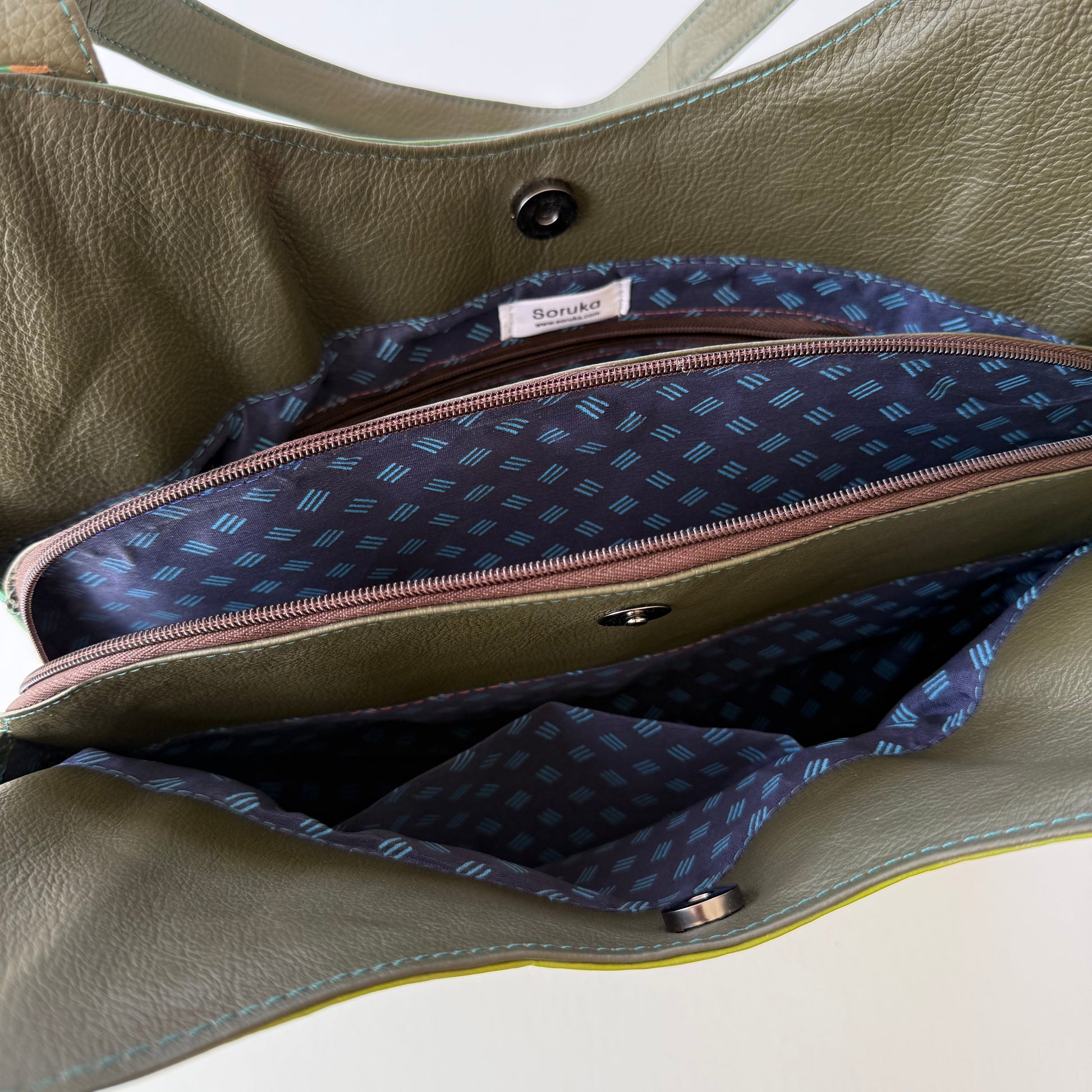 top view of green leather shoulder bag unsnapped and unzipped showing blue patterned lining