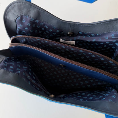 top view of blue leather shoulder bag unsnapped and unzipped showing blue patterned interior