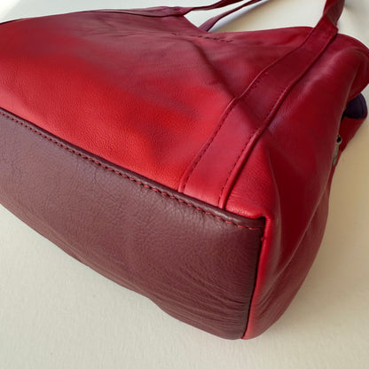 close-up of bottom of Red leather bag on a light beige surface