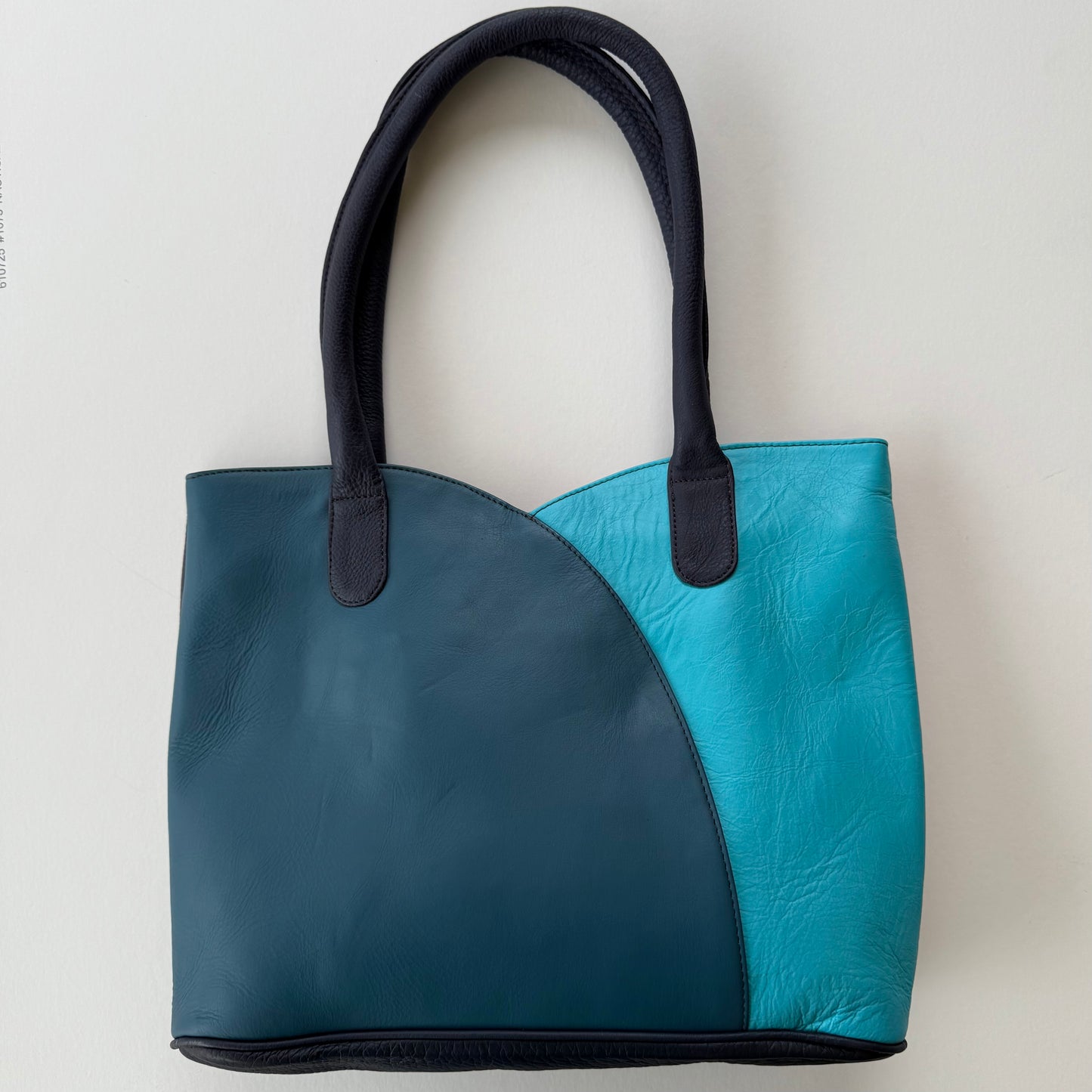 Two-toned blue handbag with black handles on a light gray background
