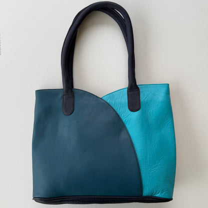 Two-toned blue handbag with black handles on a light gray background