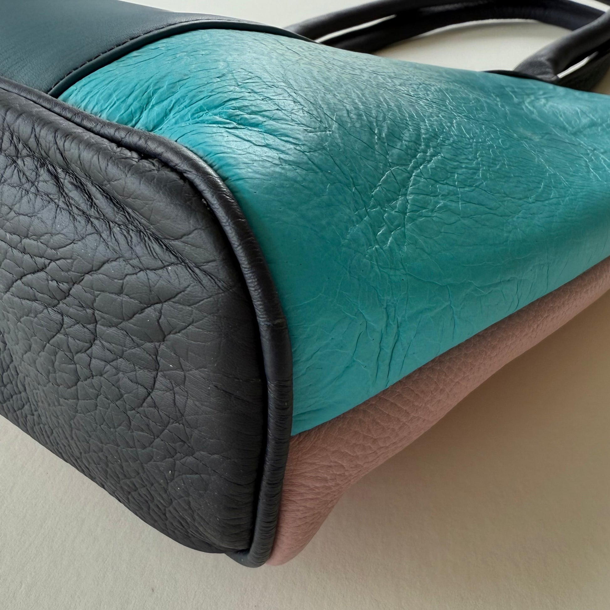 Close-up of bottom of teal and black leather handbag