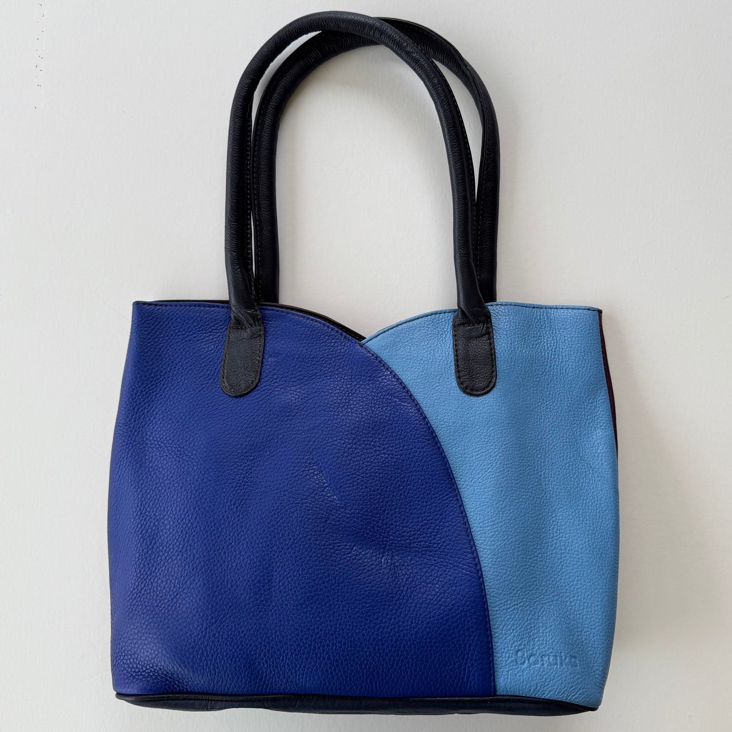 2 tone Blue tote bag with black handles on a light gray background