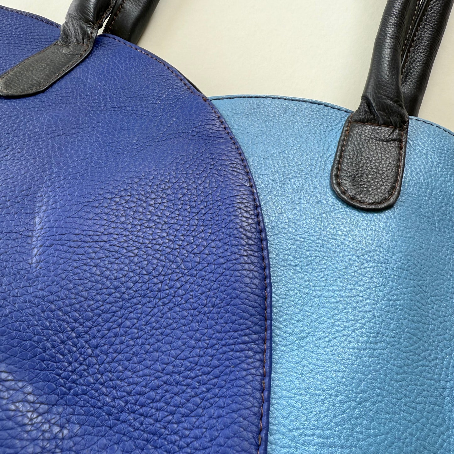 Close-up of a blue leather bag with a black strap.