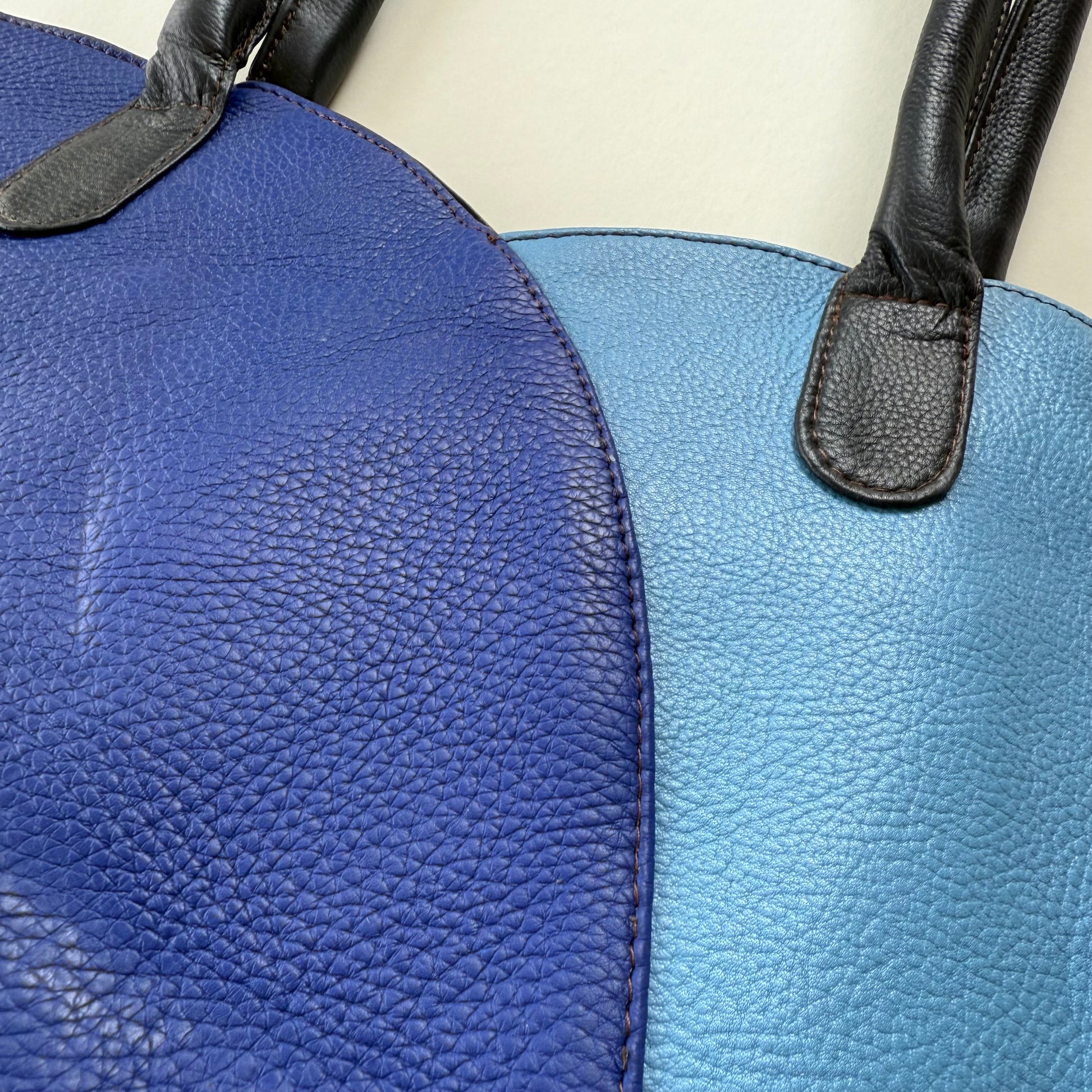Close-up of a blue leather bag with a black strap.