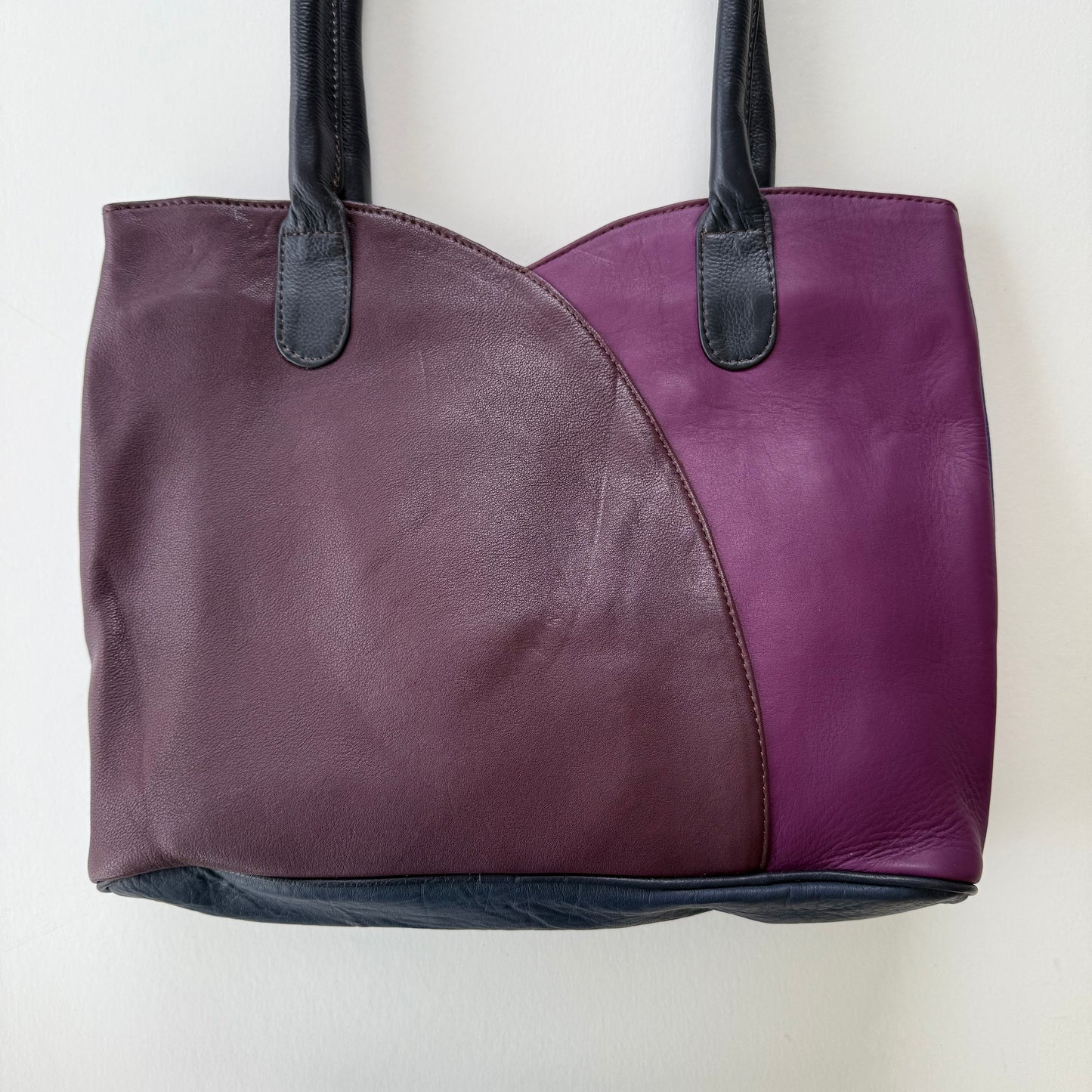 Two-tone purple handbag with black handles on a white background