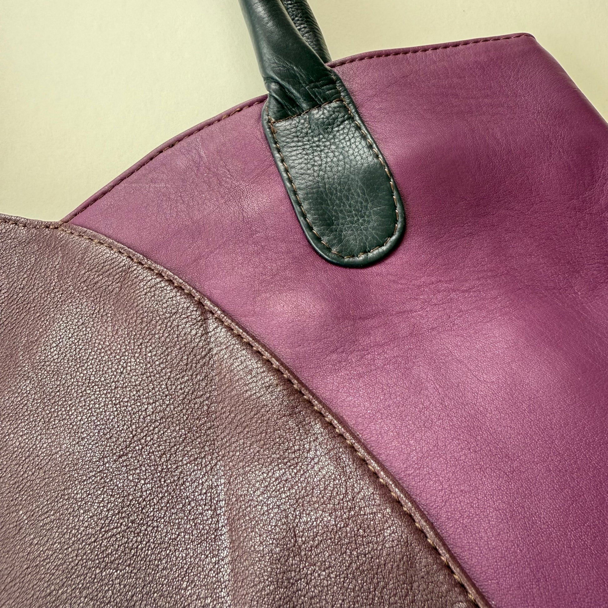 Close-up of a leather handbag with 2 purple sections on a beige background