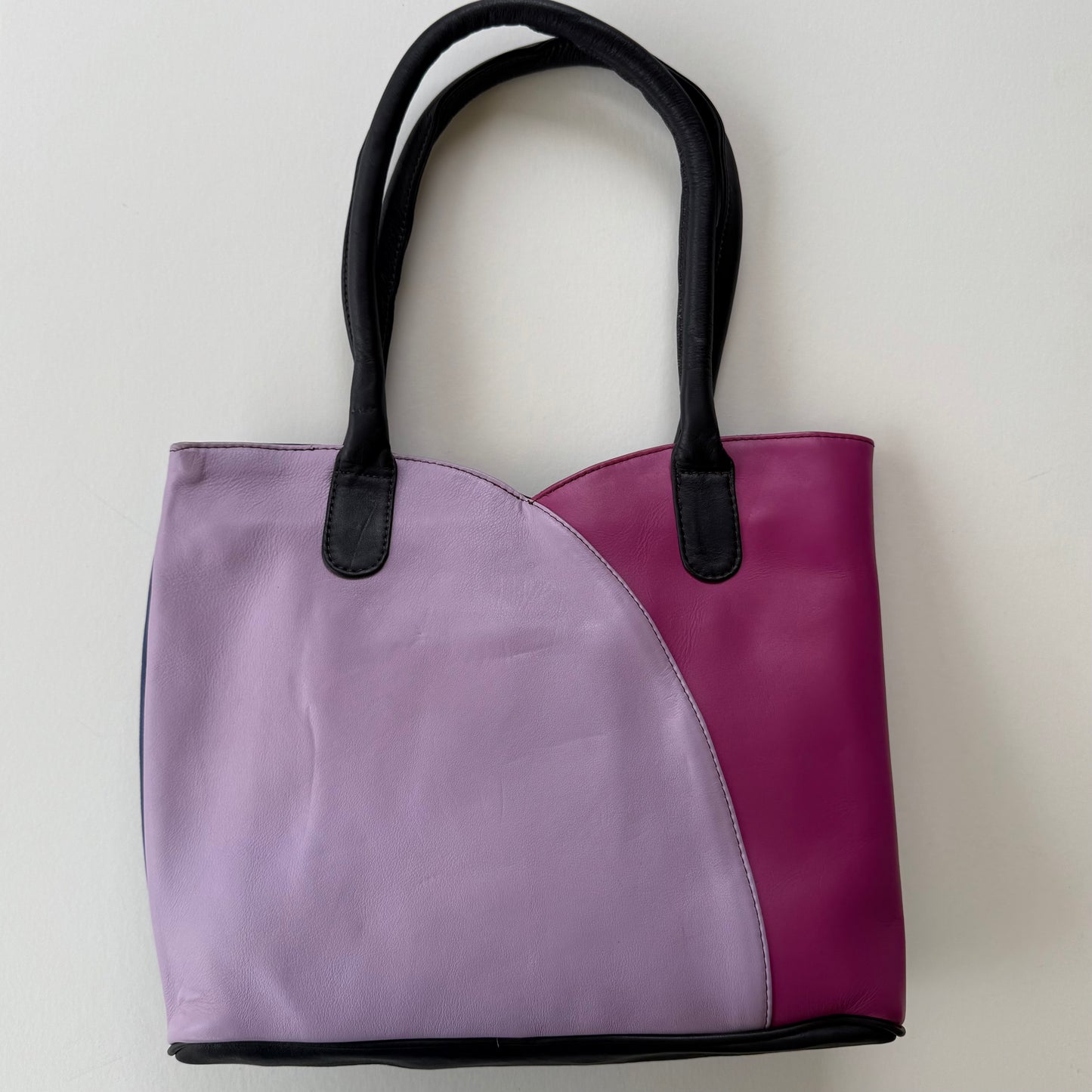 Two-toned purple and pink tote bag with black handles on a light gray background