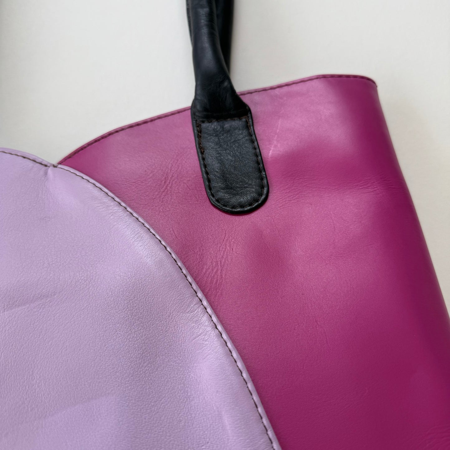 Close-up of a purple leather handbag with a black handle on a light background