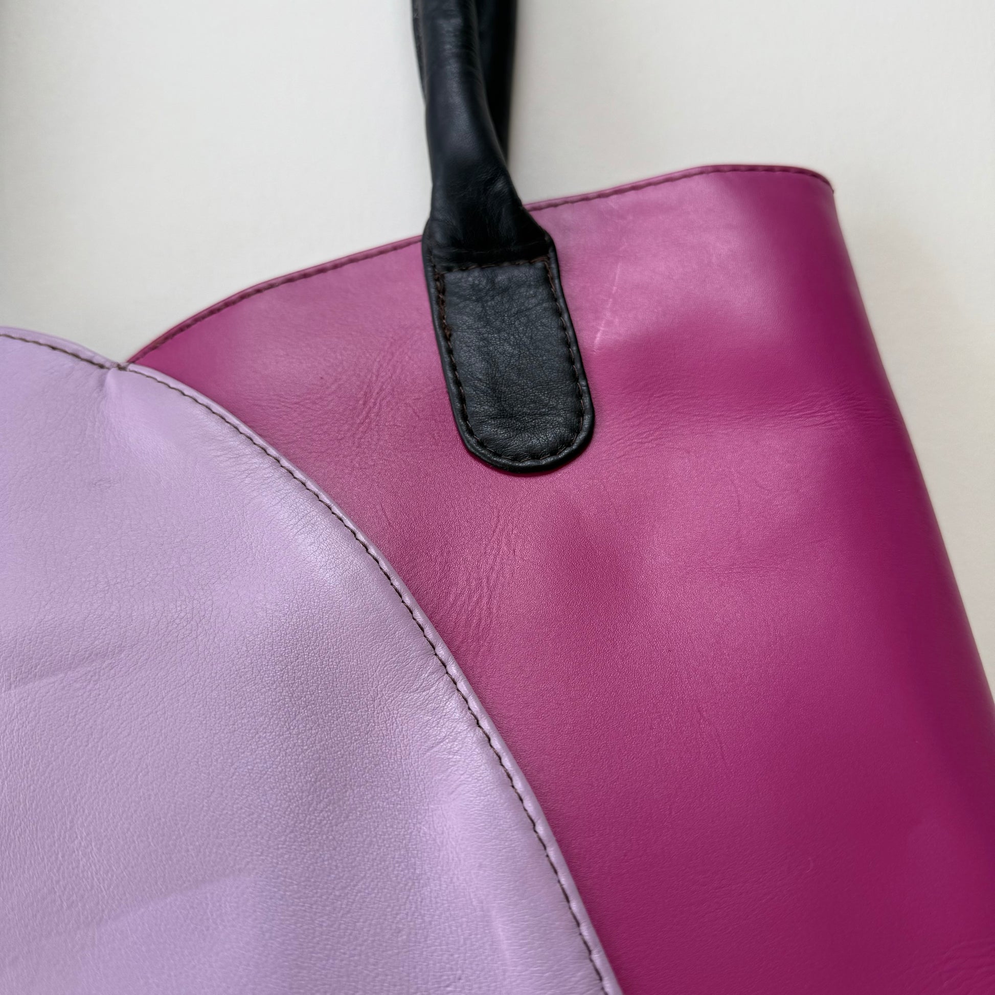 Close-up of a purple leather handbag with a black handle on a light background