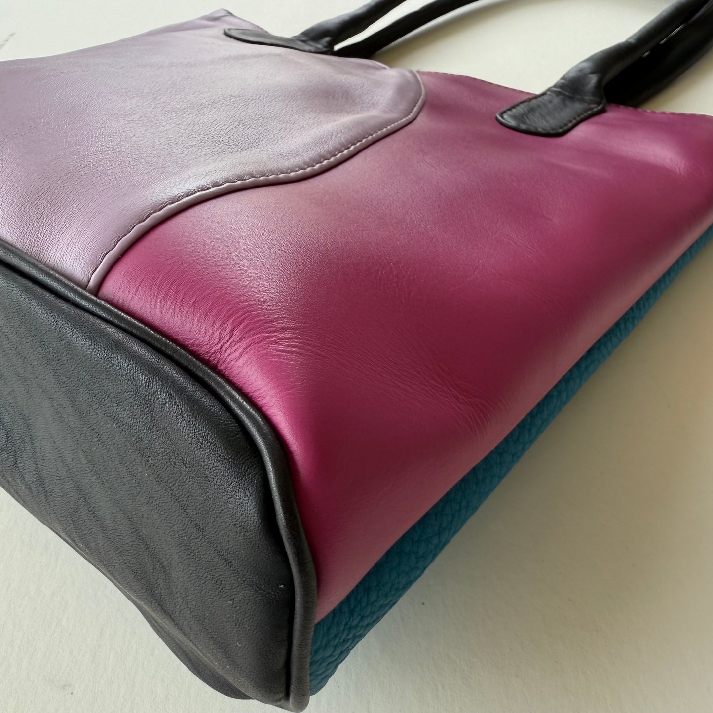 bottom view of Multicolored leather bag with purple, black, and teal sections on a light background