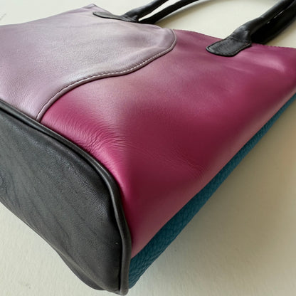 bottom view of Multicolored leather bag with purple, black, and teal sections on a light background