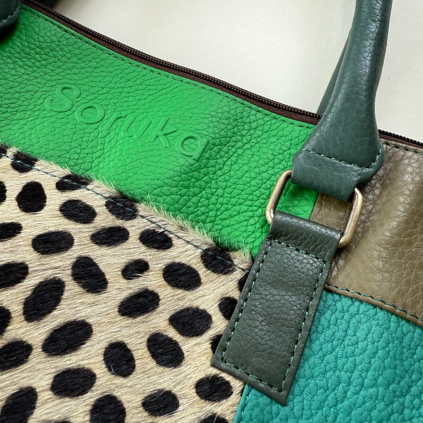 Close-up of a green leather bag  featuring a strap and a patterned section.