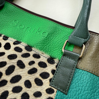 Close-up of a green leather bag  featuring a strap and a patterned section.