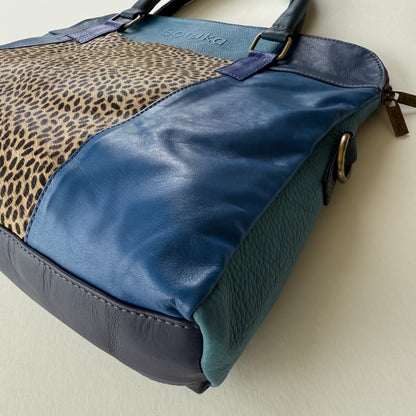 side view of Blue handbag with leopard print section on a light background